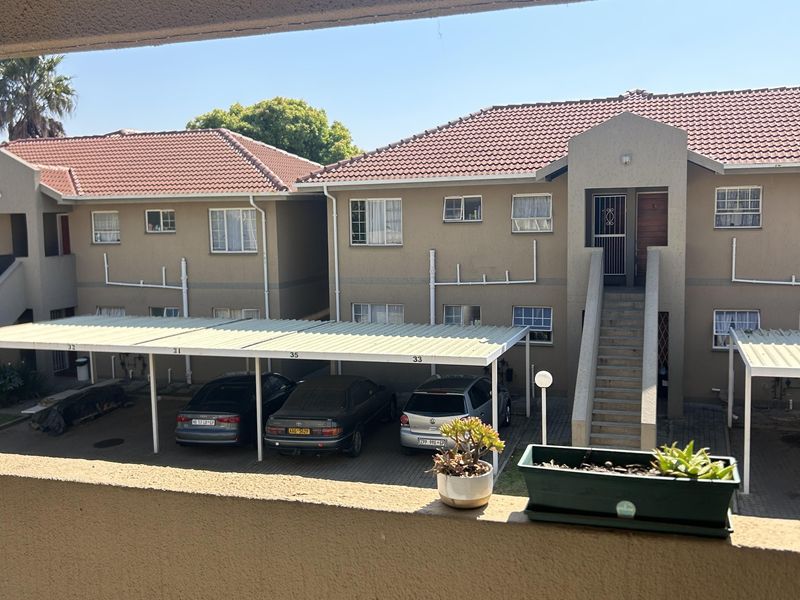 View from a balcony overlooking the apartment complex courtyard, featuring covered parking bays, tiled roof structures, and external staircases.