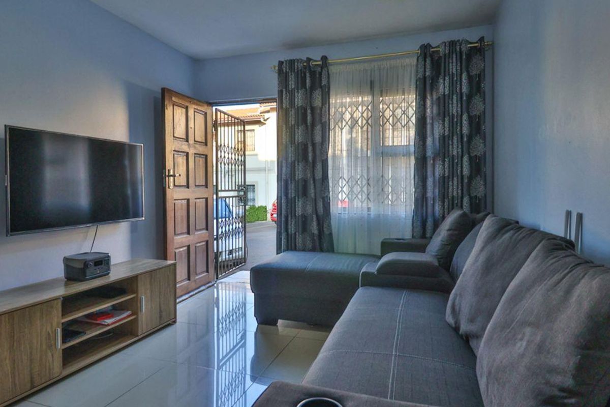 A living room featuring tiled flooring, a timber entrance door with a security gate, and a window fitted with security bars.