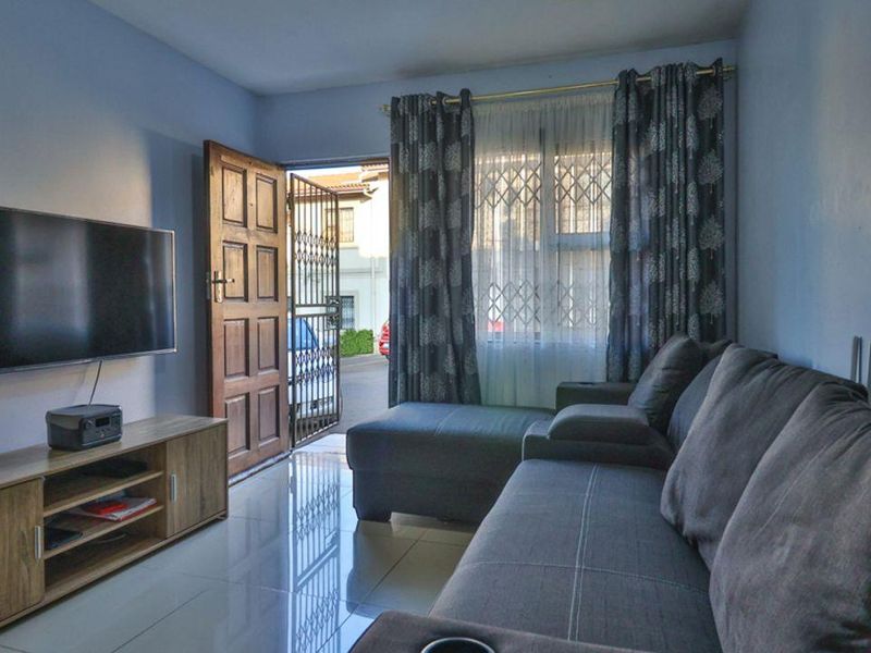 A living room featuring tiled flooring, a timber entrance door with a security gate, and a window fitted with security bars.