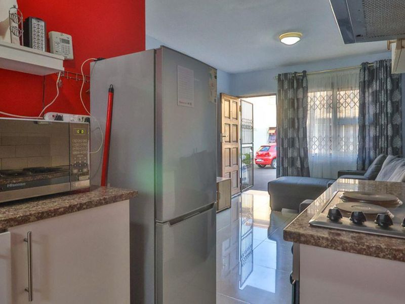 Open-plan kitchen and living area featuring granite countertops, electric hob, tiled flooring, and direct access to the exterior through a security gate.