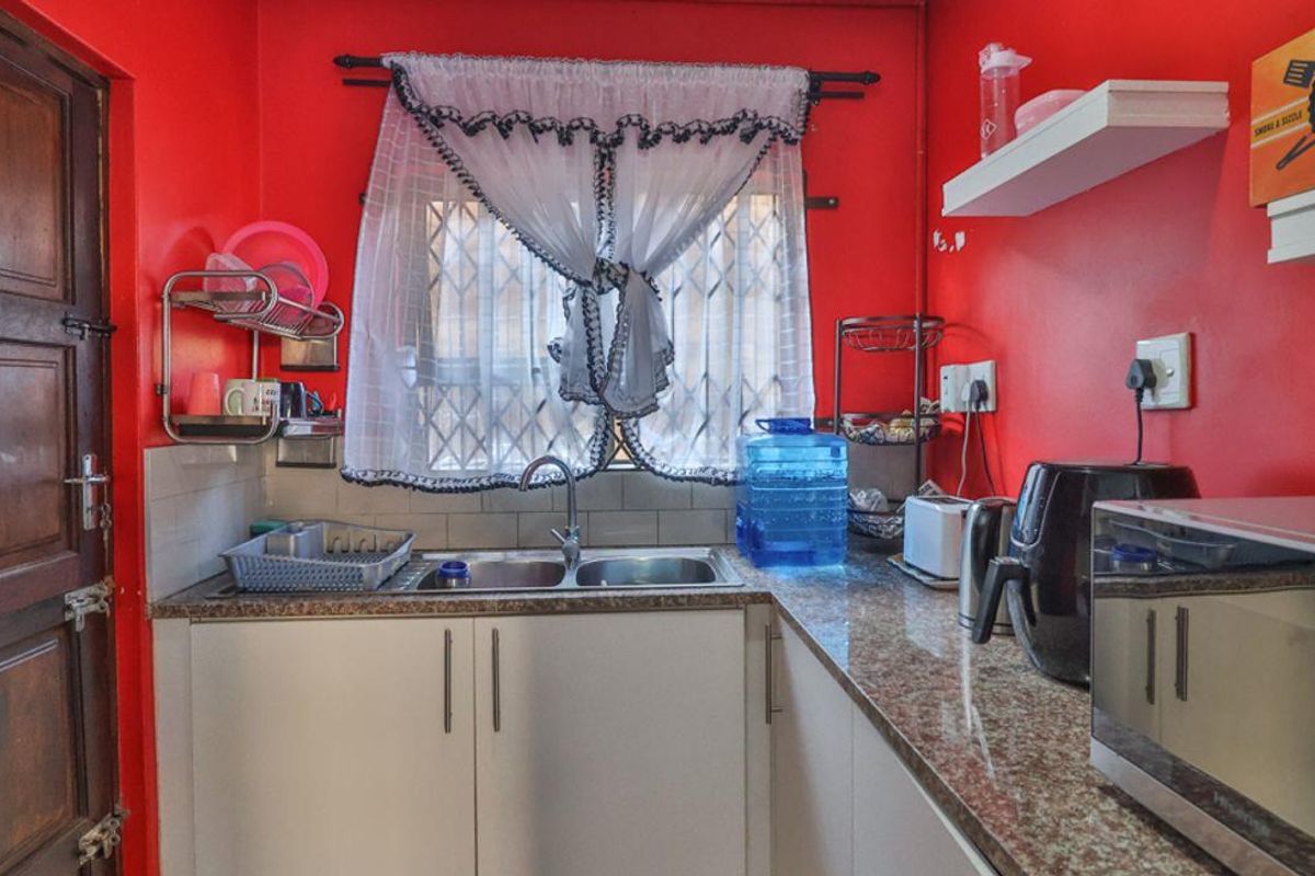 A compact kitchen featuring granite countertops, double bowl sink, and white cabinetry, currently finished with bold red wall paint.