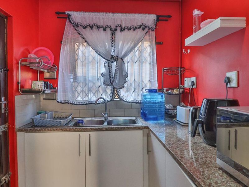 A compact kitchen featuring granite countertops, double bowl sink, and white cabinetry, currently finished with bold red wall paint.