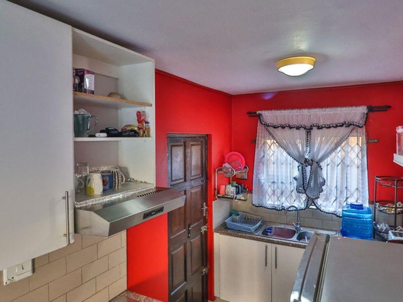 A compact kitchen featuring white cabinetry, a double bowl sink, tiled backsplash, and an extractor fan, finished with bold red wall paint.
