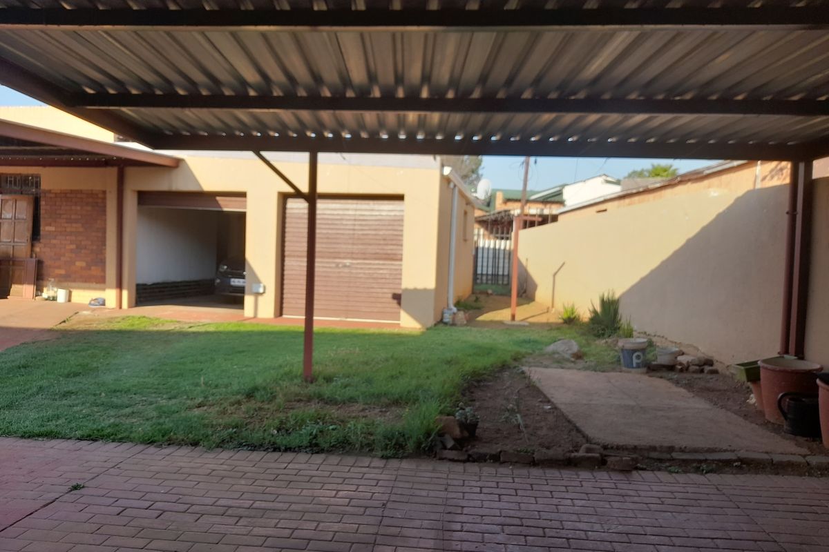 Rear exterior view featuring a covered carport, paved driveway, and a private garden area with boundary walling.