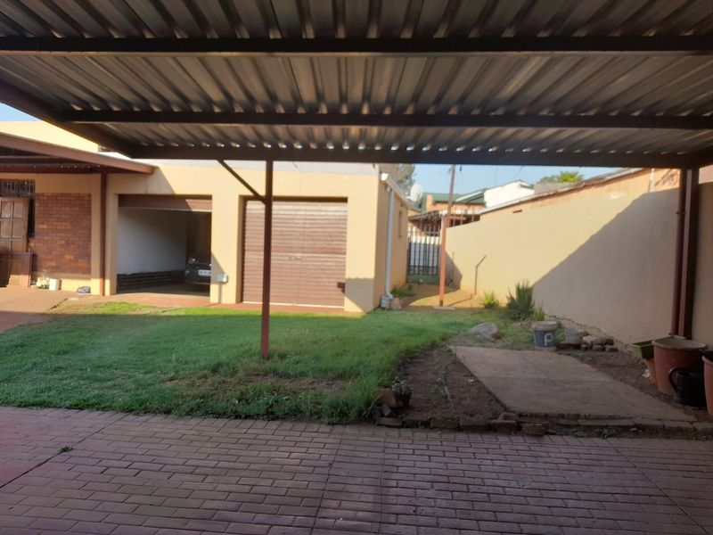 Rear exterior view featuring a covered carport, paved driveway, and a private garden area with boundary walling.