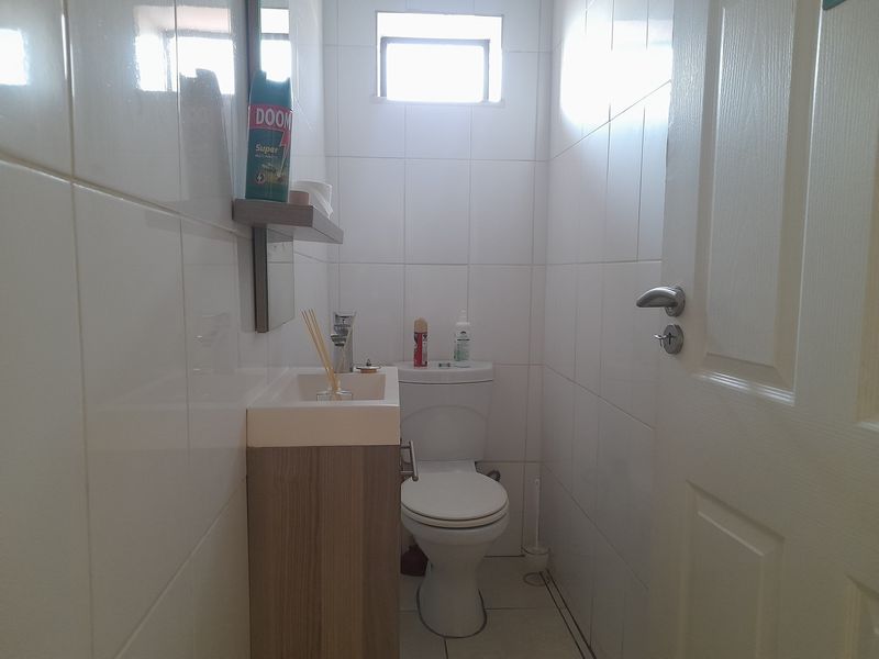 A compact guest bathroom featuring a modern vanity unit, toilet, and full-height white wall tiling.