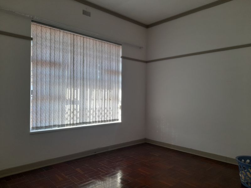 An empty bedroom featuring polished parquet flooring, neutral walls with picture rails, and vertical window blinds.