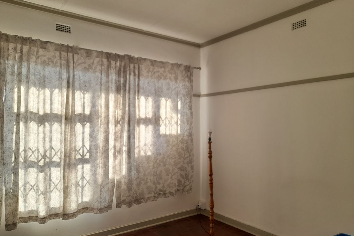 A bright, empty bedroom featuring original parquet flooring, picture rails, and security bars on the windows, offering a clean canvas for personalization.
