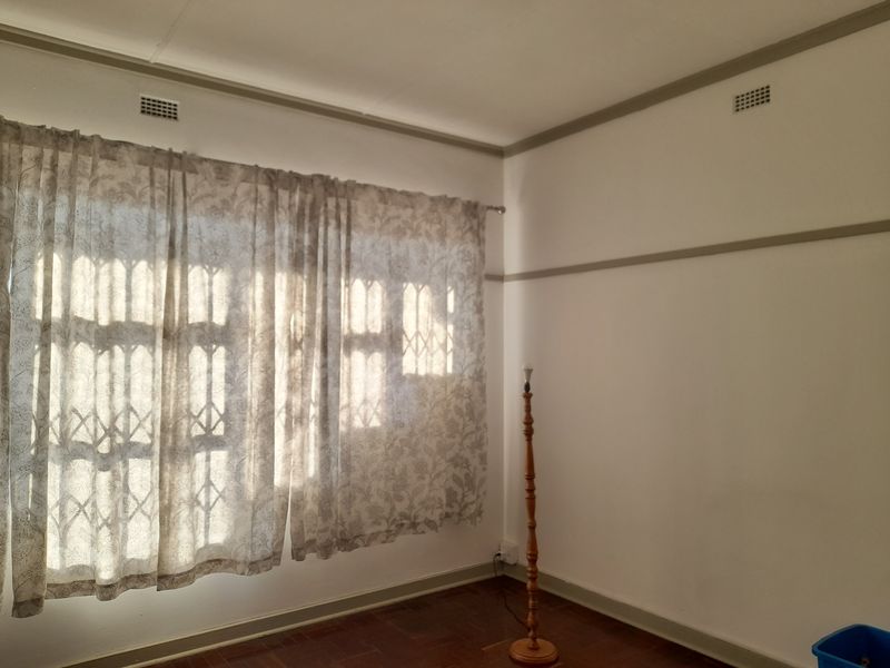 A bright, empty bedroom featuring original parquet flooring, picture rails, and security bars on the windows, offering a clean canvas for personalization.