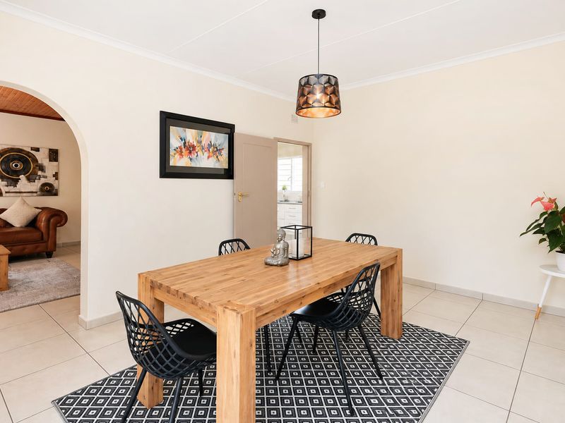 A bright dining room featuring neutral tiled flooring, a decorative archway leading to an adjacent living space, and a modern pendant light fixture.