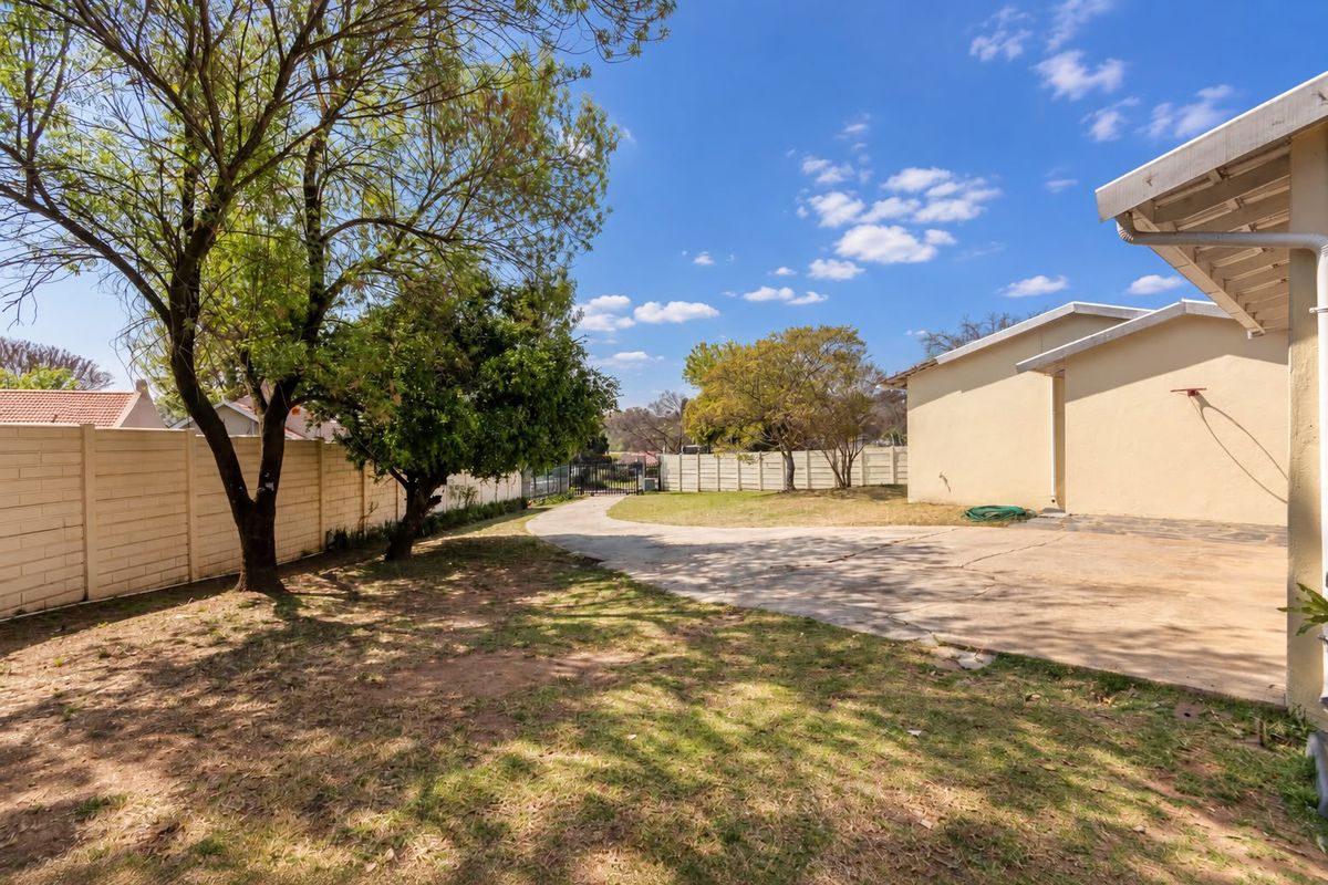 Spacious rear yard featuring a concrete driveway, established trees, and secure perimeter walling, offering potential for landscaping or outdoor development.