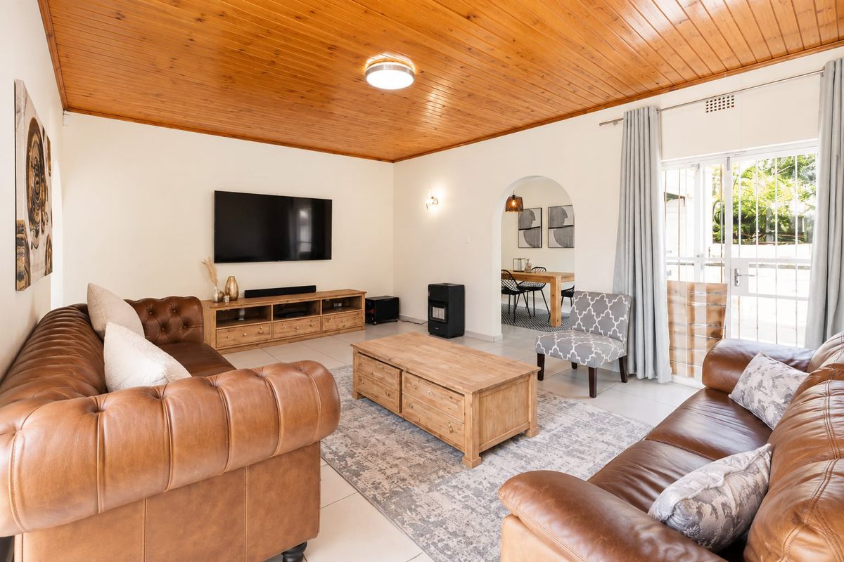 Spacious living room featuring a warm timber tongue and groove ceiling, tiled flooring, and an elegant archway leading to the dining area.