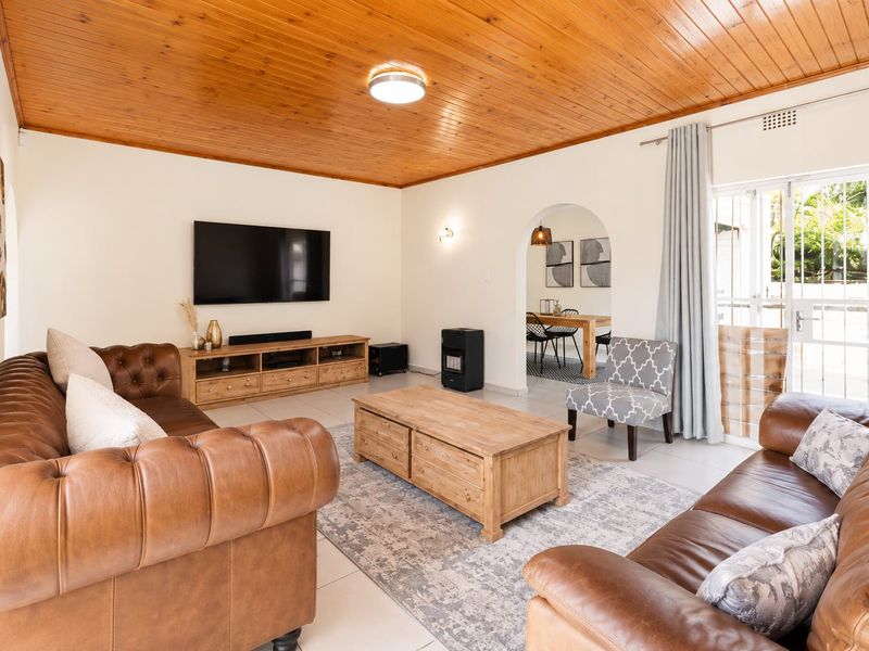 Spacious living room featuring a warm timber tongue and groove ceiling, tiled flooring, and an elegant archway leading to the dining area.