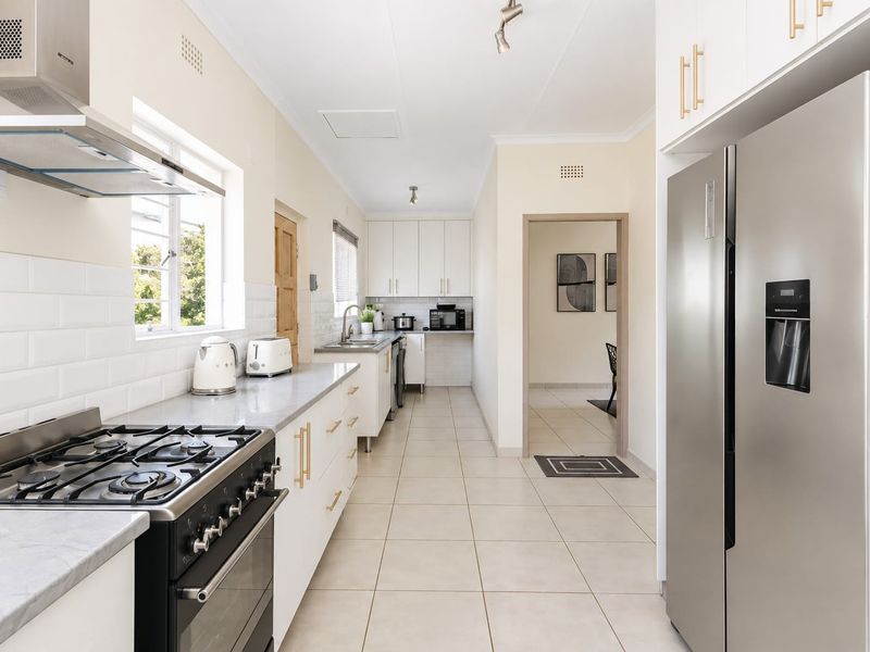 A bright, modern kitchen featuring white cabinetry, subway tile backsplash, a gas stove with extractor, and neutral floor tiles.