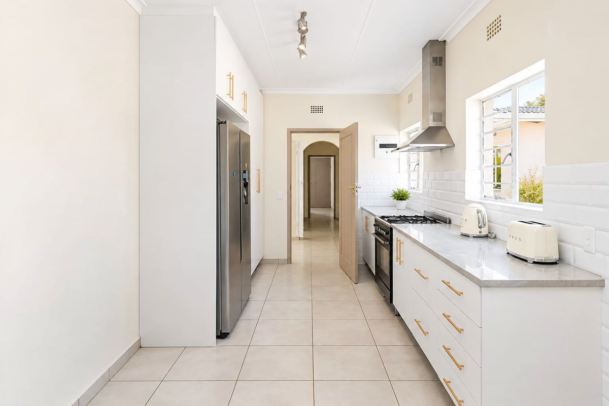 Modern kitchen featuring white cabinetry, stone countertops, subway tile backsplash, and stainless steel appliances, leading into a central hallway.