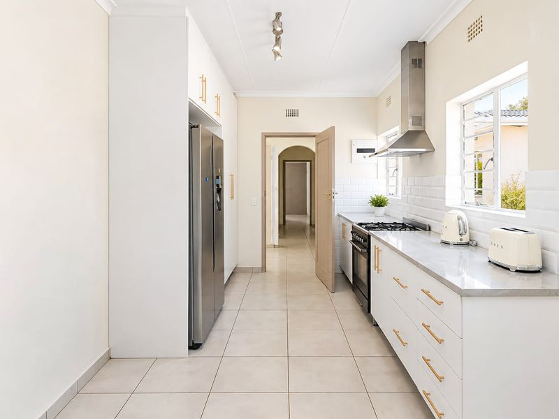 Modern kitchen featuring white cabinetry, stone countertops, subway tile backsplash, and stainless steel appliances, leading into a central hallway.