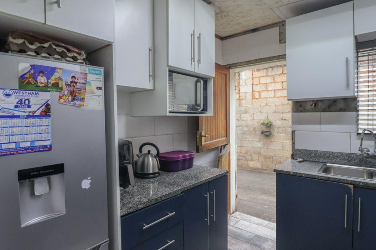 Compact kitchen featuring granite countertops, dark blue lower cabinetry, white upper cabinets, and a stainless steel double sink with direct access to an exterior area.