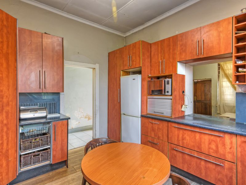 A dated kitchen featuring wood-look laminate cabinetry, dark countertops, and a built-in microwave, with visible wear on the surrounding wall surfaces.