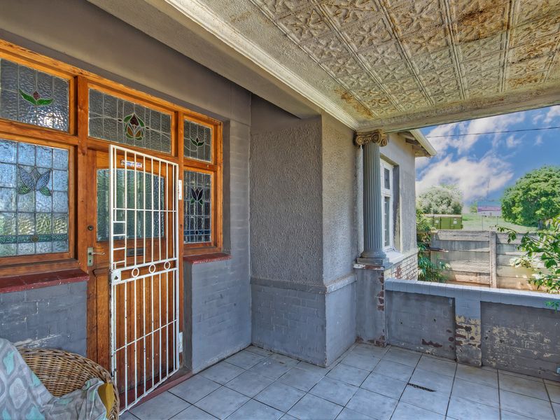 Covered front patio featuring decorative ceiling tiles, a classical column, and stained glass window detailing, requiring some maintenance to the masonry and ceiling finishes.