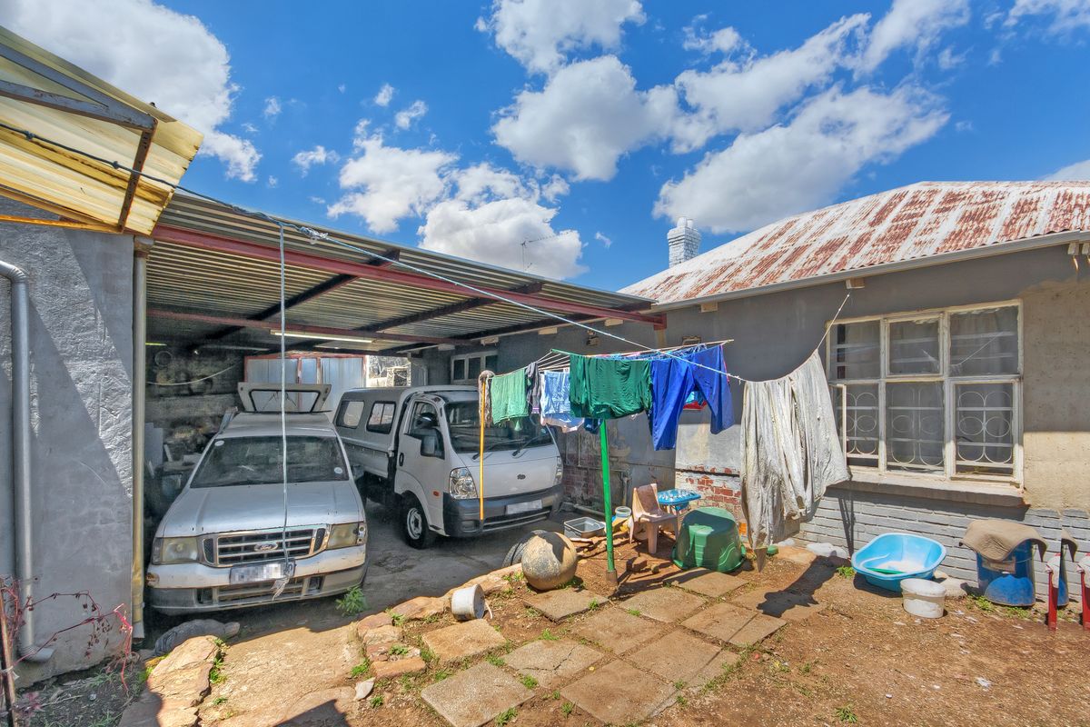 Rear exterior view of the property featuring a carport structure and a main building with a weathered corrugated metal roof and brick facade.