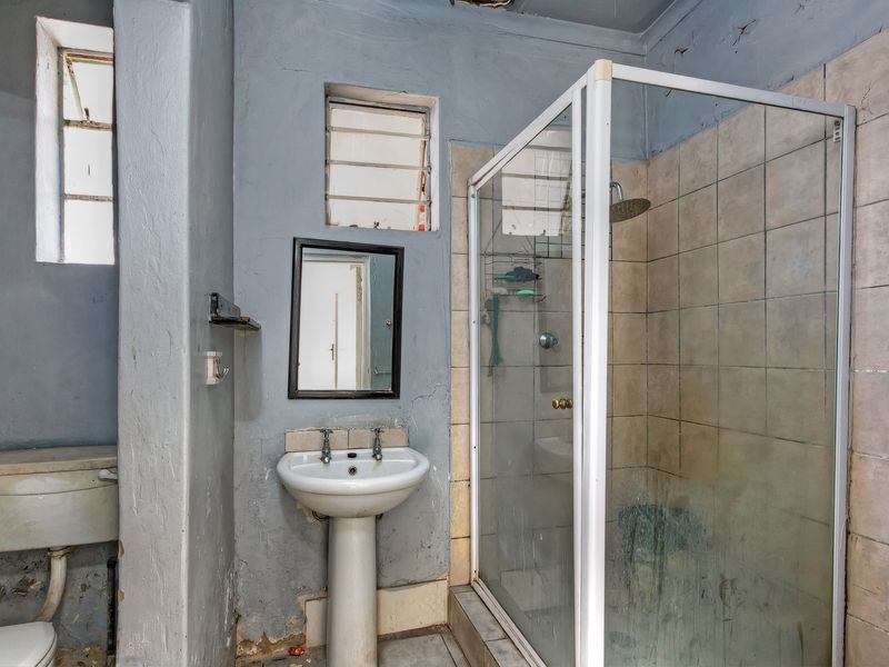 A dated bathroom featuring a pedestal basin, shower enclosure, and toilet. The space requires significant renovation and cosmetic updates to improve its condition.