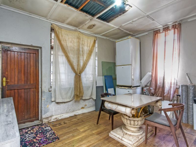 A kitchen space in need of significant renovation, featuring timber flooring, original timber door, and damaged ceiling panels requiring repair.