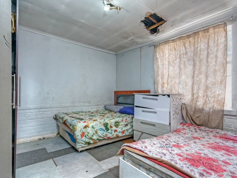 A bedroom featuring exposed brickwork and a built-in wardrobe, currently requiring significant ceiling and wall repairs to restore the space.