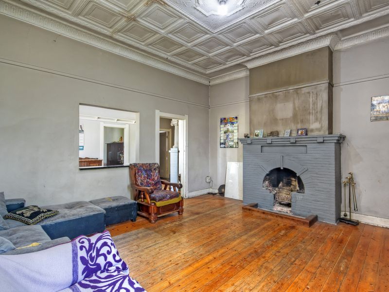 Spacious living room featuring original pressed metal ceilings, timber flooring, and a prominent brick fireplace, offering significant potential for renovation and modernization.