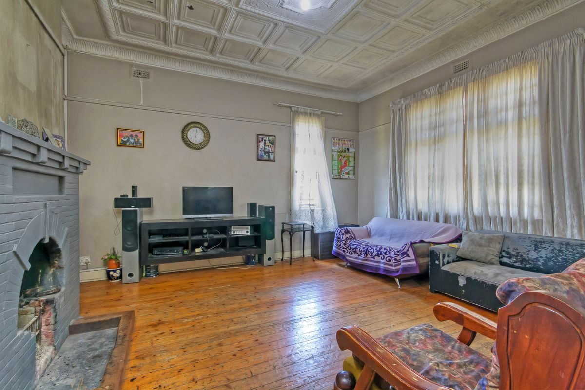 Spacious living room featuring original pressed metal ceilings, timber flooring, and a character brick fireplace, offering significant potential for renovation and restoration.