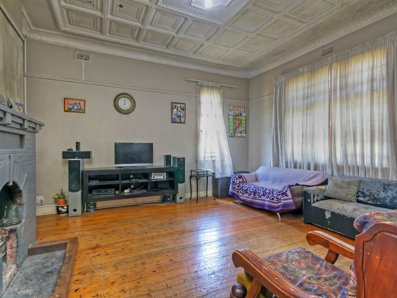 Spacious living room featuring original pressed metal ceilings, timber flooring, and a character brick fireplace, offering significant potential for renovation and restoration.