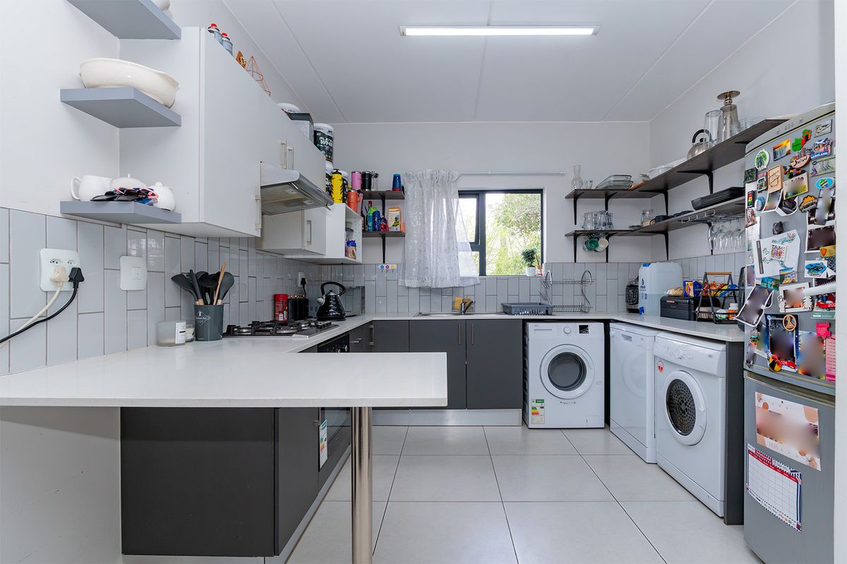 Modern kitchen featuring grey and white cabinetry, tiled backsplash, gas hob, and integrated laundry facilities with ample counter space and open shelving.