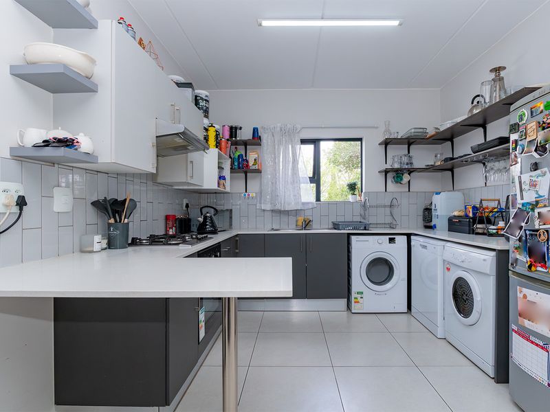 Modern kitchen featuring grey and white cabinetry, tiled backsplash, gas hob, and integrated laundry facilities with ample counter space and open shelving.
