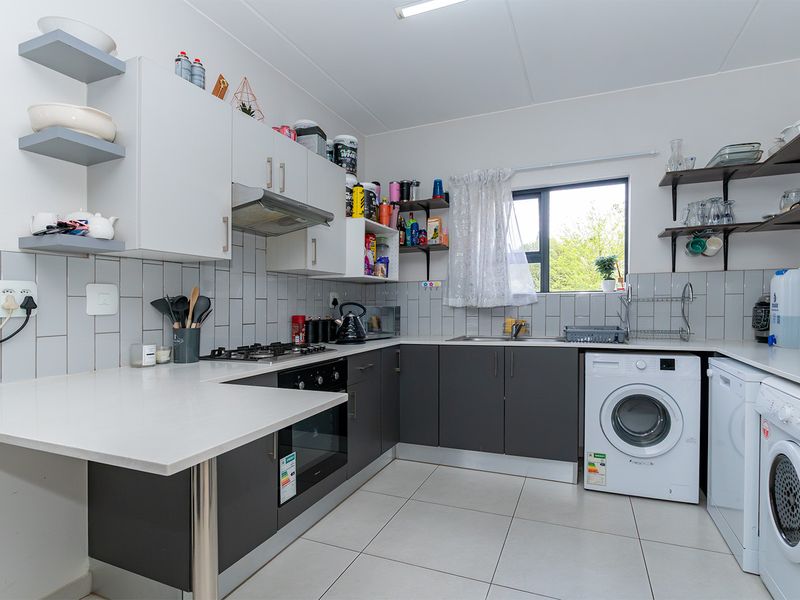A functional kitchen featuring dark grey lower cabinetry, white upper cabinets, a gas hob, built-in oven, and integrated laundry appliance connections.