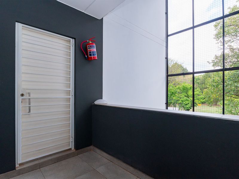A clean, modern balcony area featuring tiled flooring, a secure metal gate, and a large window overlooking greenery.