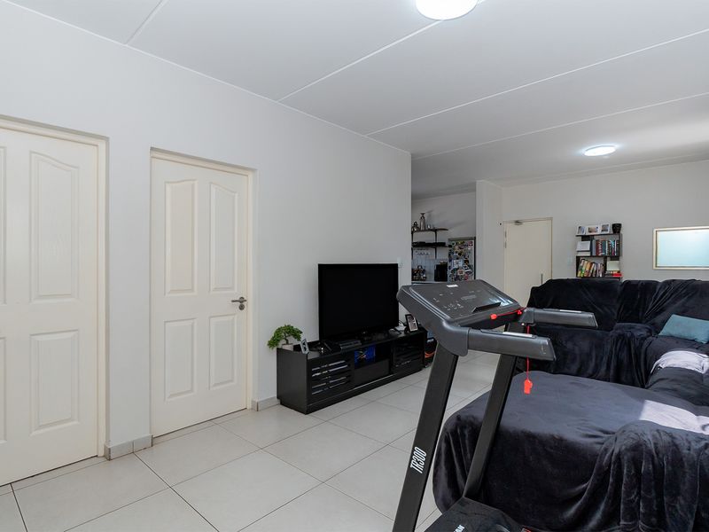 A spacious living area featuring neutral tiled flooring, panel doors, and recessed ceiling lighting, offering a functional and versatile layout for daily living.