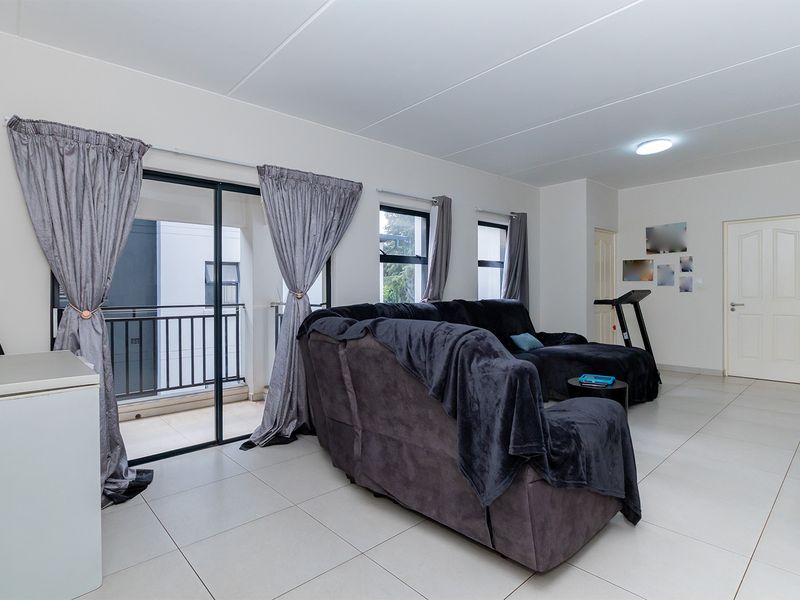A spacious living area featuring neutral tiled flooring and a sliding glass door providing direct access to a private balcony.
