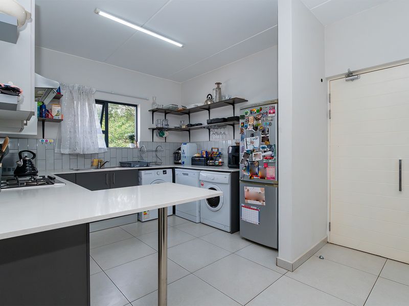 Functional kitchen featuring dark cabinetry, white countertops, gas hob, and integrated laundry plumbing, providing a practical workspace with tiled finishes.