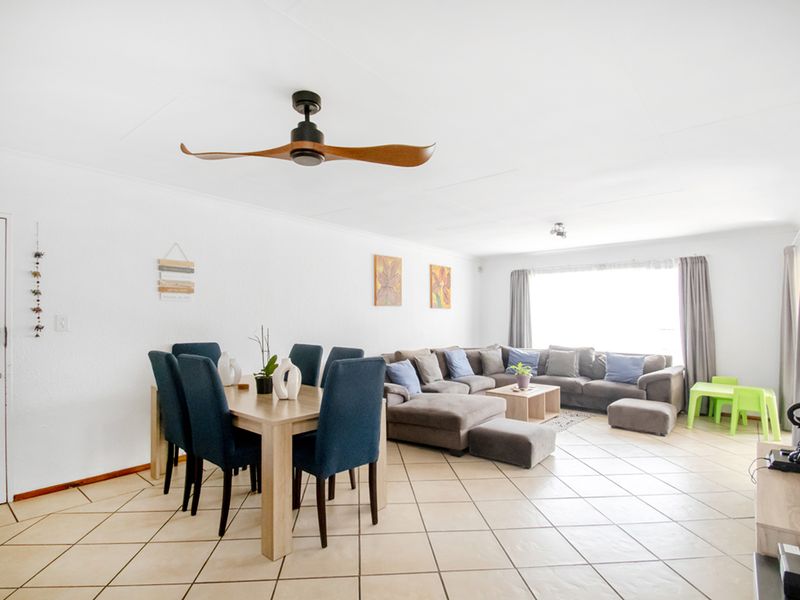 Spacious open-plan living and dining area featuring neutral tiled flooring, a modern ceiling fan, and large windows providing ample natural light.