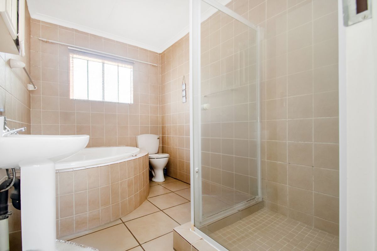 A functional bathroom featuring a built-in bathtub, a separate tiled shower enclosure, a pedestal basin, and a toilet with neutral wall and floor tiling.