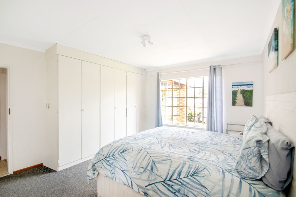 A well-lit bedroom featuring built-in cupboards, neutral wall finishes, and a large grid-pattern window allowing for natural light.