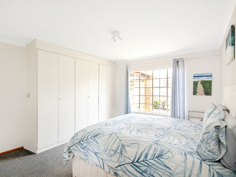 A well-lit bedroom featuring built-in cupboards, neutral wall finishes, and a large grid-pattern window allowing for natural light.