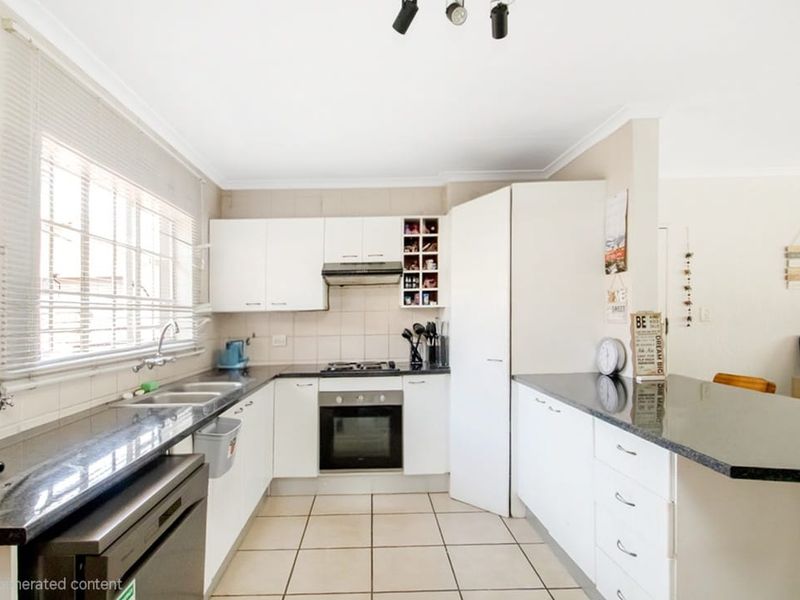A functional kitchen featuring white cabinetry, dark granite countertops, tiled flooring, and integrated appliances including a gas hob and oven.