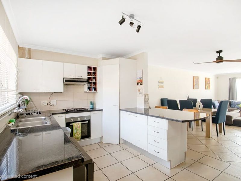 Open-plan kitchen and living area featuring white cabinetry, granite countertops, built-in appliances, and tiled flooring throughout the space.