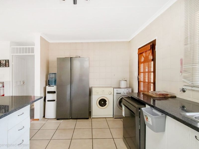 Functional kitchen featuring granite countertops, tiled splashbacks, and tiled flooring, with integrated space for laundry appliances and direct access to the exterior.