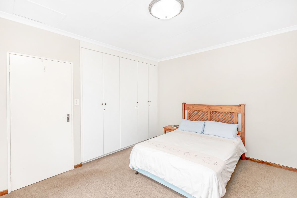 A well-lit bedroom featuring neutral walls, carpeted flooring, and extensive built-in cupboard storage.