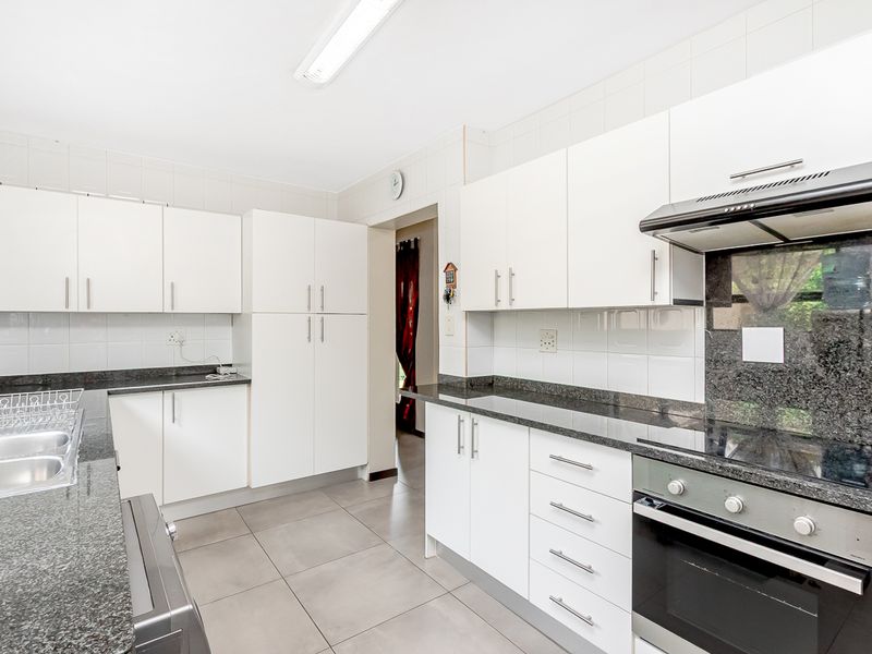 A clean, functional kitchen featuring white cabinetry, granite countertops, a built-in oven, and an electric hob with an extractor fan.