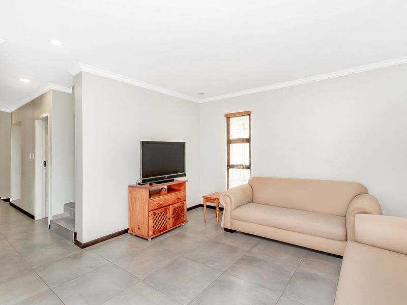 A bright living room featuring neutral tiled flooring, recessed downlighting, and clean wall finishes, providing a versatile space for relaxation.