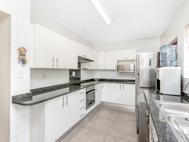 A functional kitchen featuring white cabinetry, granite countertops, tiled splashbacks, and integrated appliances including an oven, hob, and extractor fan.