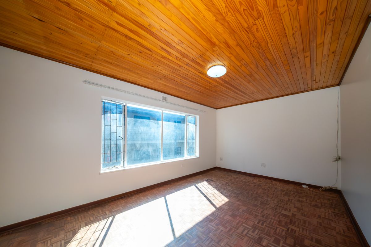 An empty bedroom featuring classic parquet flooring and a warm wooden tongue and groove ceiling, providing a neutral canvas for interior design.