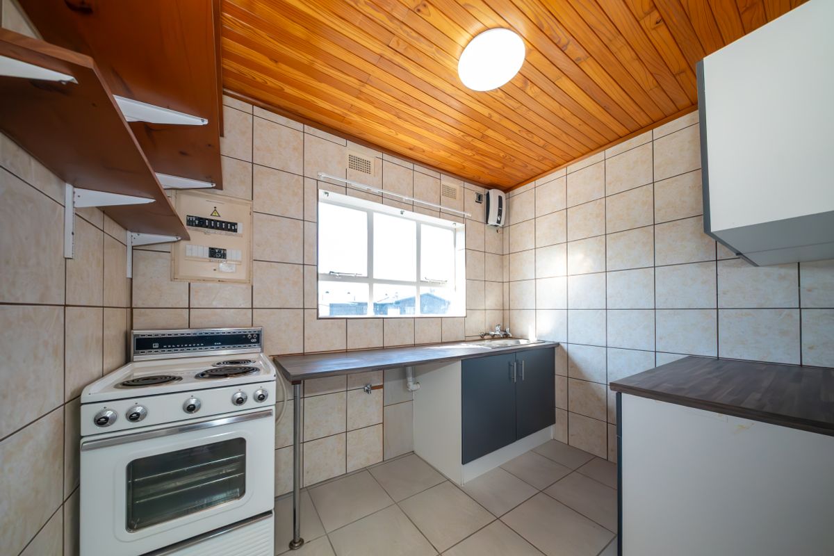A functional kitchen featuring tiled walls and flooring, a timber ceiling, built-in cabinetry with laminate countertops, and an electric stove.